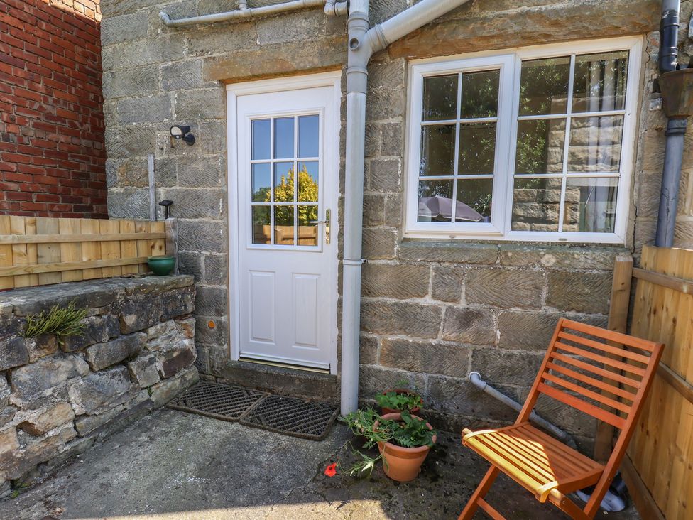 An outdoor area with a door, windows, a chair and a flower pot at 4 Lilac Cottages in Ainthorpe