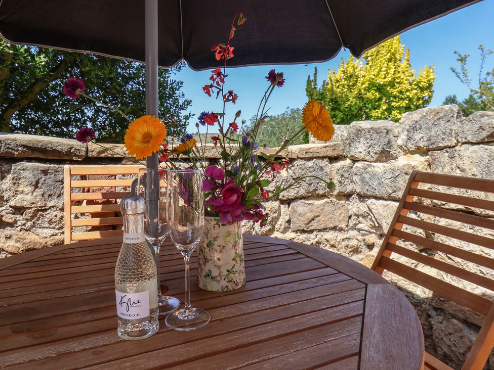 An outdoor dining area with a table, chairs, flowers, and drinks at 4 Lilac Cottages Ainthorpe