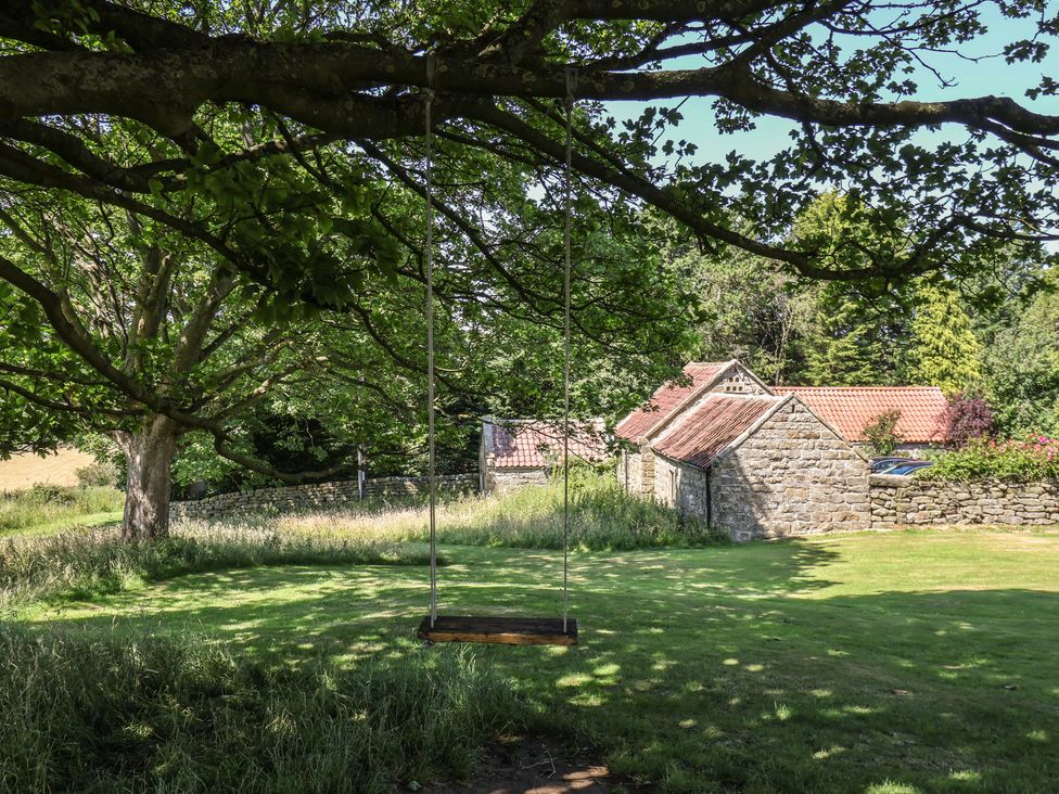 A swing hanging from a tree near stone buildings at 4 Lilac Cottages Ainthorpe