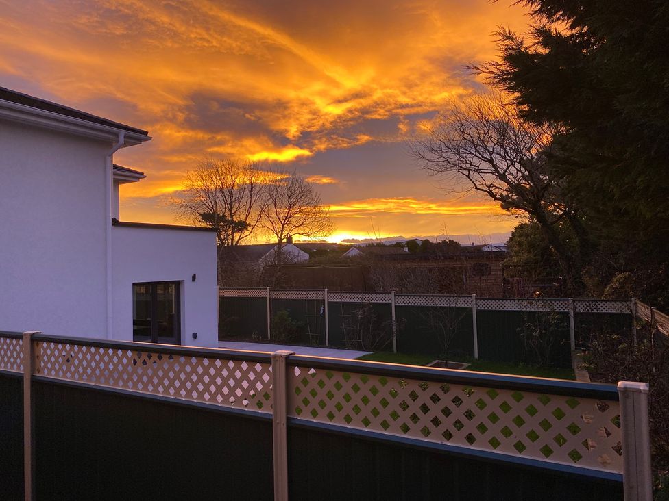 A garden with a fence and sunset view at Pityme-Not in Wadebridge