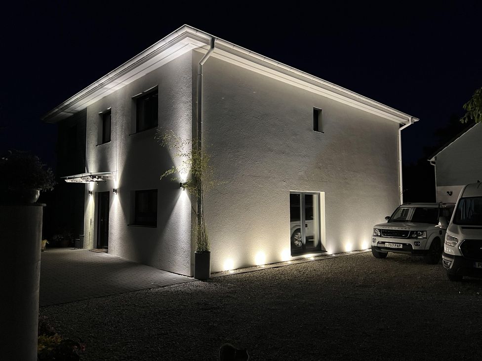 A house with lights illuminating the entrance and parked cars at Pityme-Not in Wadebridge