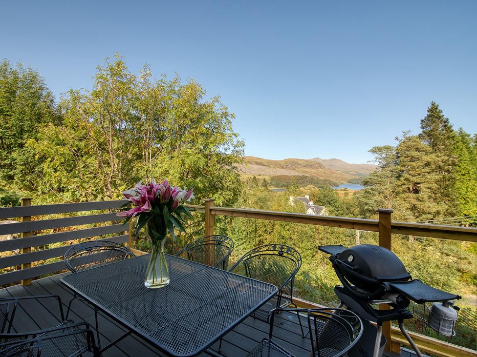 A deck area with a table, chairs and flowers at Pinemarten Lodge in Crianlarich