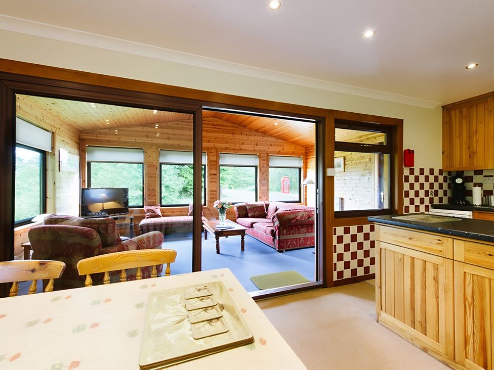 A kitchen with a table and chairs and a view to a living area at Buzzard Lodge in Crianlarich