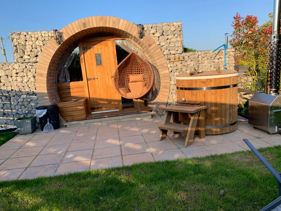 An outdoor area with a wooden structure, chair, barrel, and stone wall at Cosy Escape in Sheerness