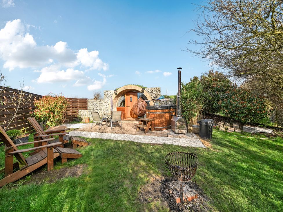 An outdoor garden with a hot tub, wooden chairs and fire pit at Cosy Escape in Minster On Sea