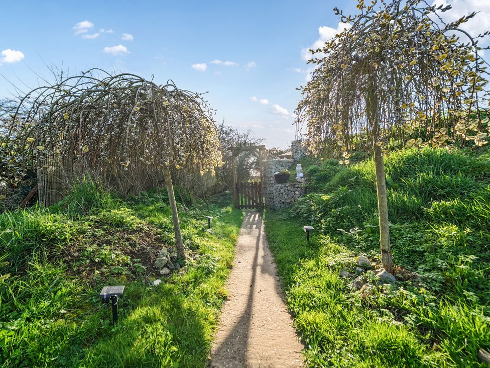 A garden pathway leading to a gate surrounded by trees at Cosy Escape Minster On Sea
