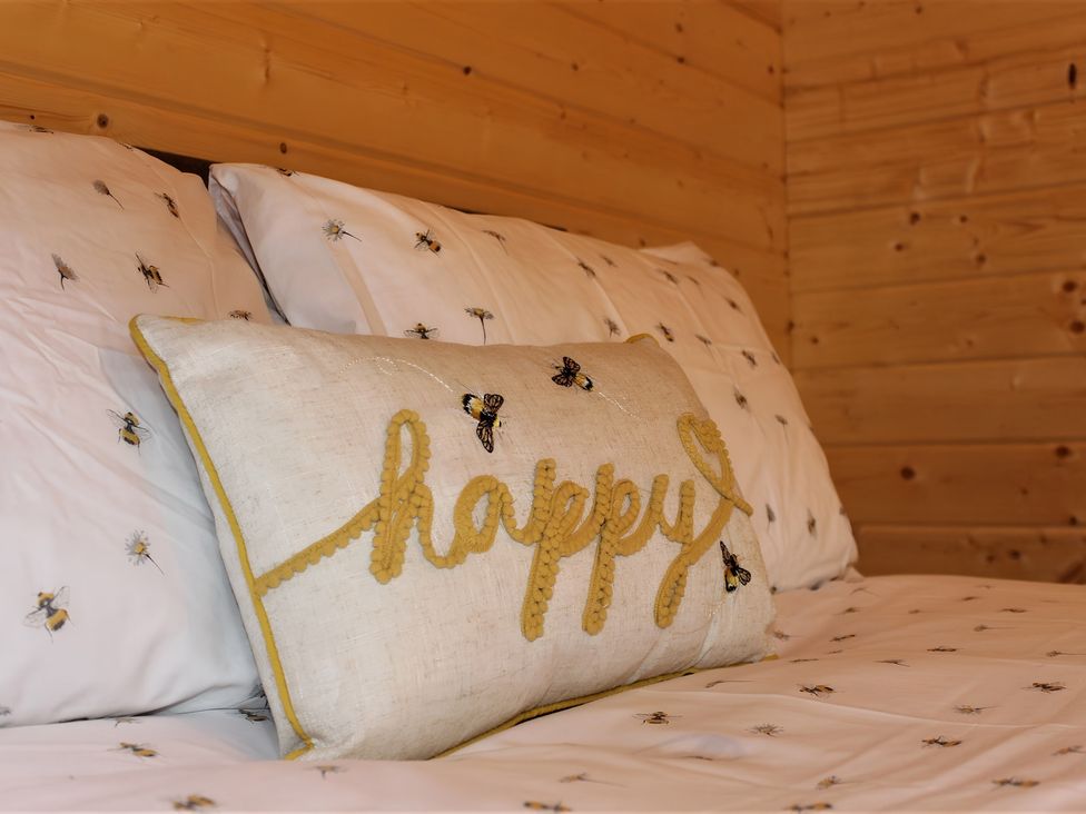 A bed with a decorative pillow and bee patterned bedding at Cotswold Nights Away Evesham