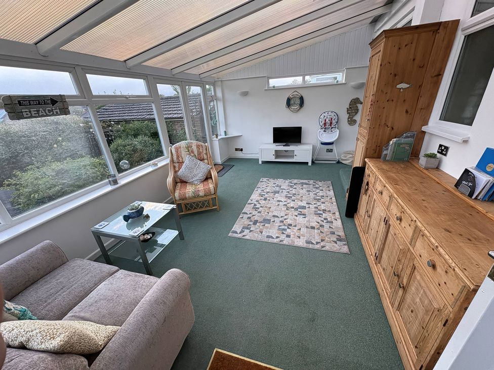 A conservatory with a sofa, armchair, coffee table, and television at Tudor Rose in Weymouth