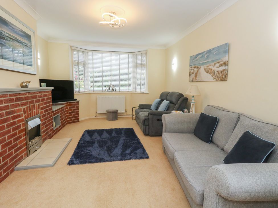 A living room with a sofa, armchair, and television at Tudor Rose in Weymouth