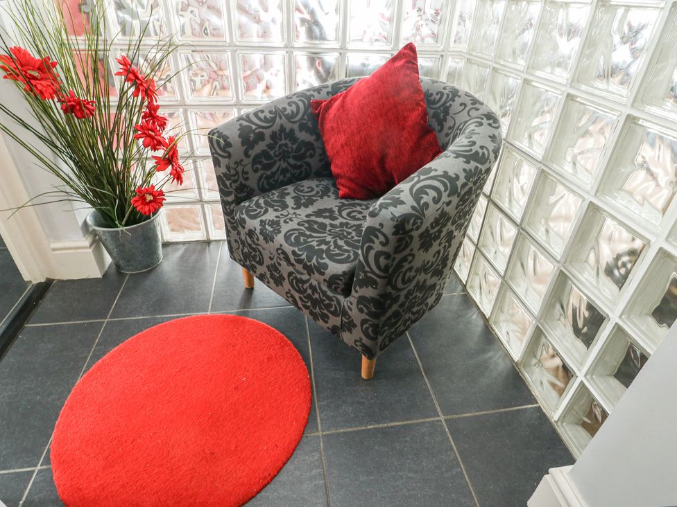 A hallway with an armchair, red cushion, and artificial flowers at Ty Llyn in Brynteg near Benllech