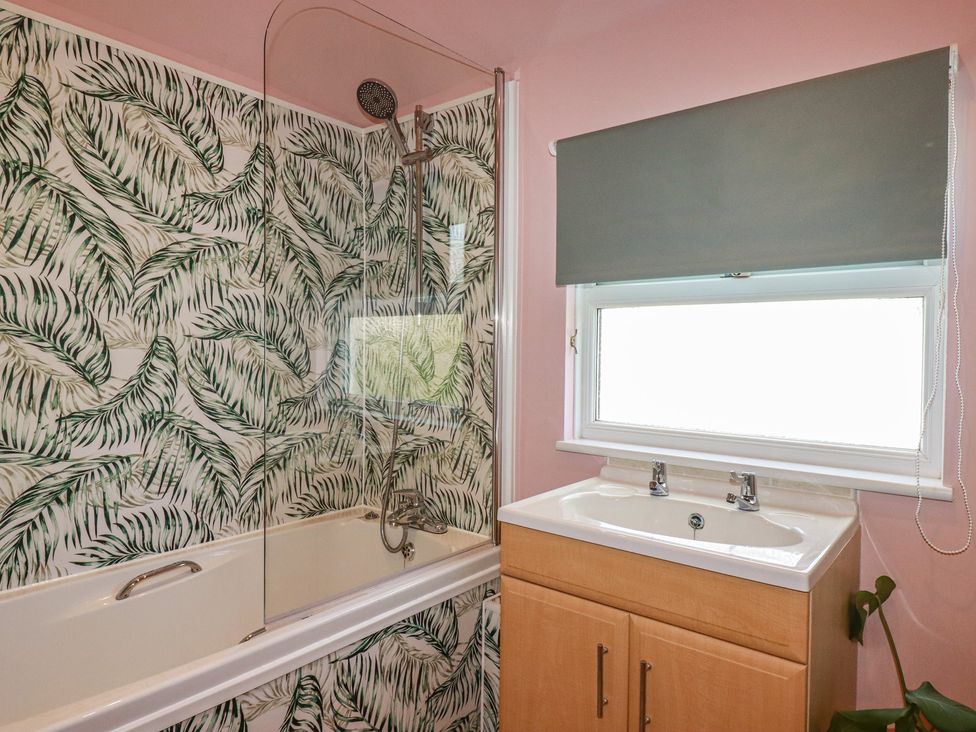 A bathroom with a bathtub, shower, sink, and window at 3A Grannys Lane, Perranporth