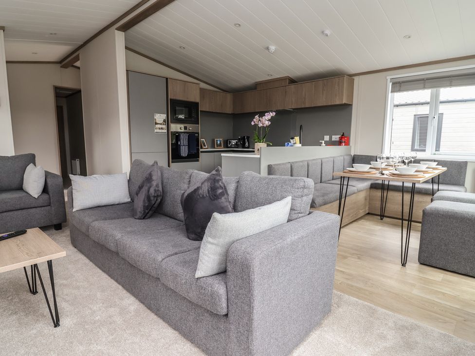 A living room with a sofa and kitchen area at Cedar Lodge 3 Bedrooms in Delamere