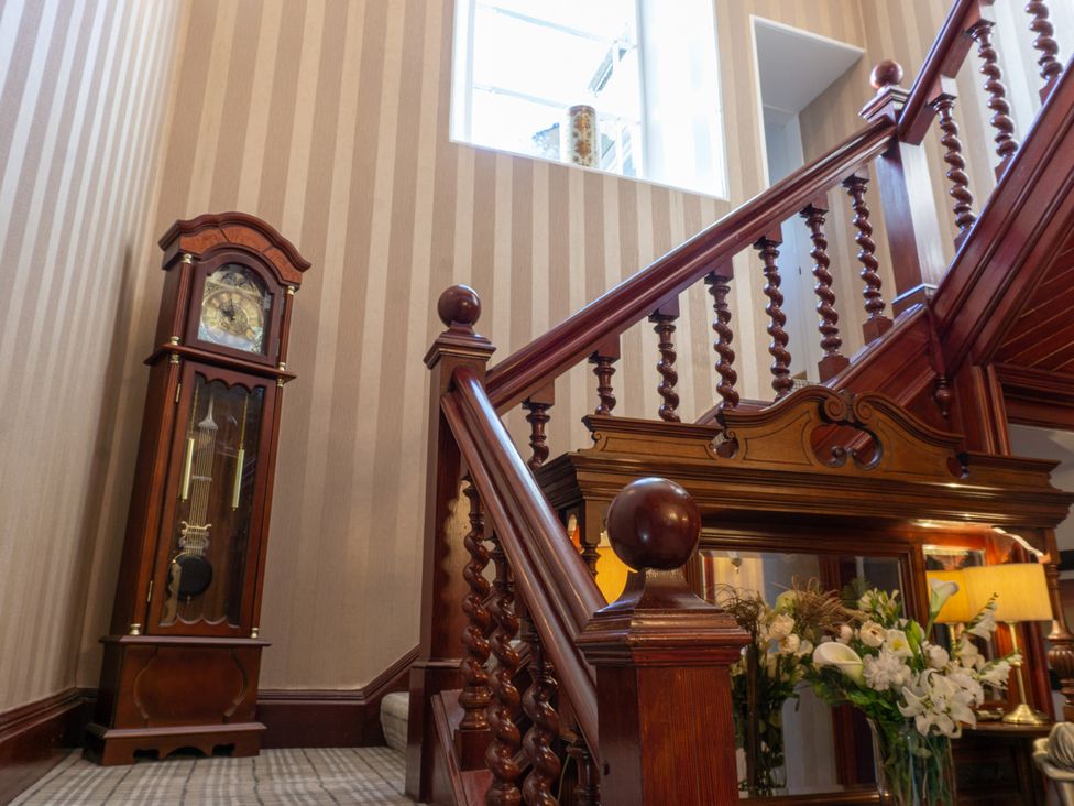 A staircase with a grandfather clock and flowers at Newton Manor House in Cupar