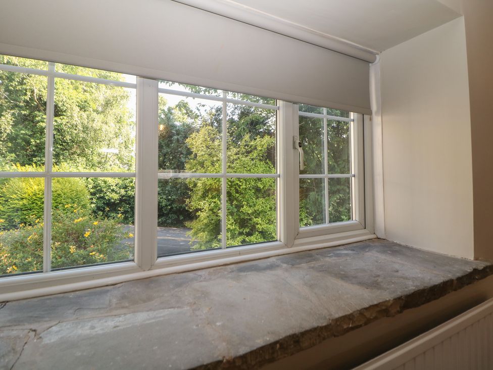 A window with a stone sill overlooking greenery at Lake Side Cottage in Wakefield