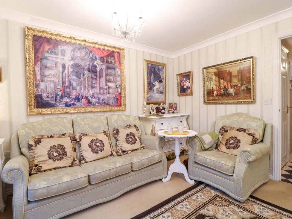 A living room with a sofa, armchairs, a coffee table and paintings at 41 Lower Birches Way Rugeley