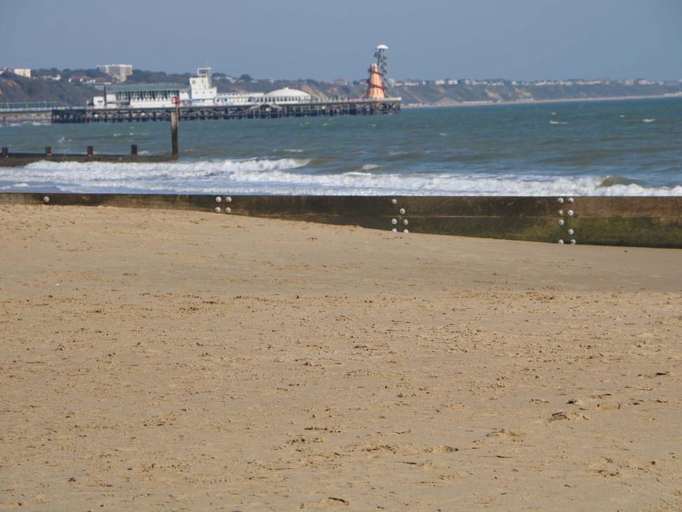A beach with sand and a pier in the background at Woodlands House in Ringwood