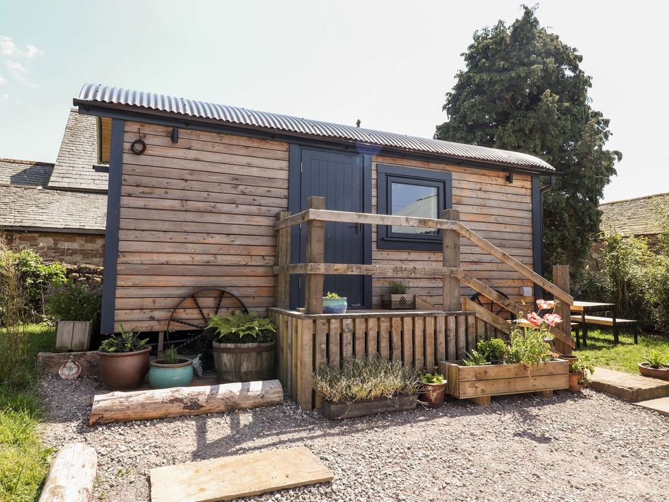 An exterior view of a wooden hut with steps and garden features at Dunfell Shepherd's Hut in Appleby-In-Westmorland