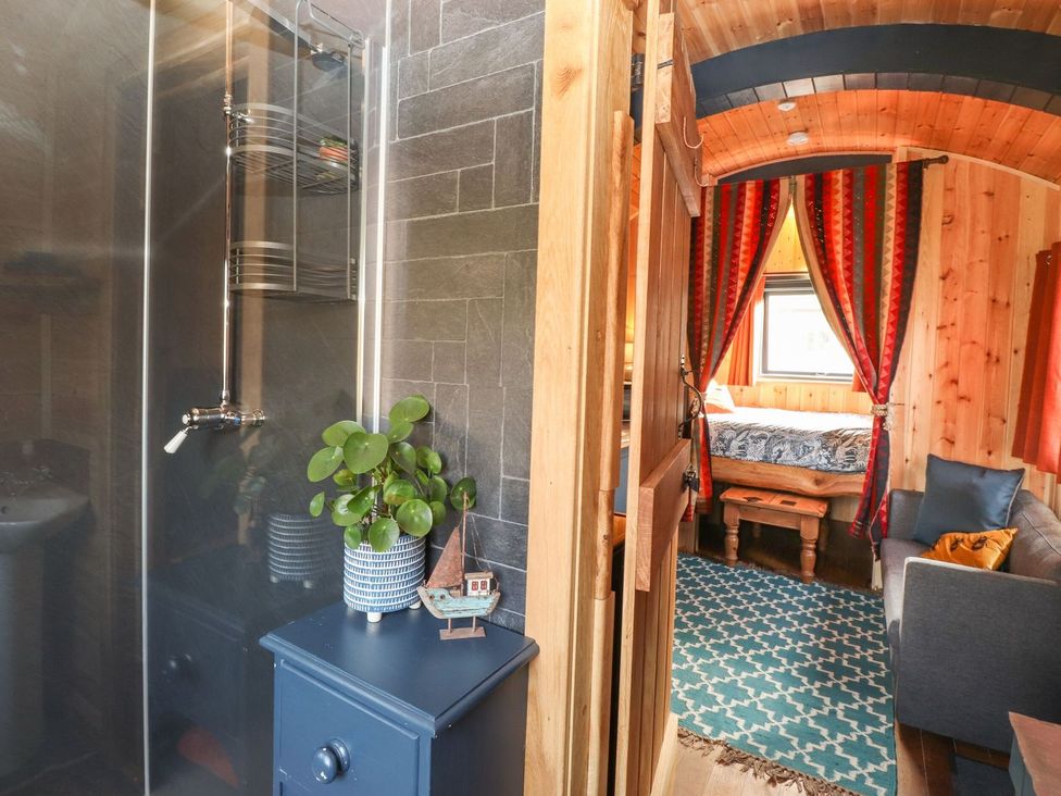 A bathroom with a shower and a visible room with a bed and sofa at Dunfell Shepherd's Hut in Appleby-In-Westmorland