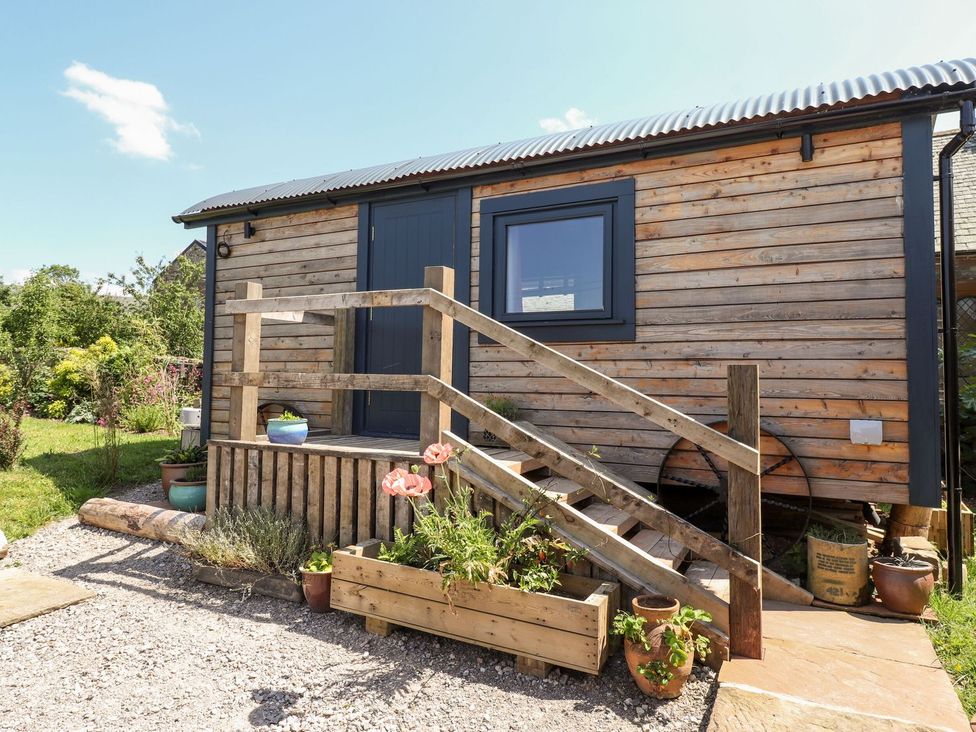 An outdoor view of a wooden structure with steps and garden features at Dunfell Shepherd's Hut Appleby-In-Westmorland