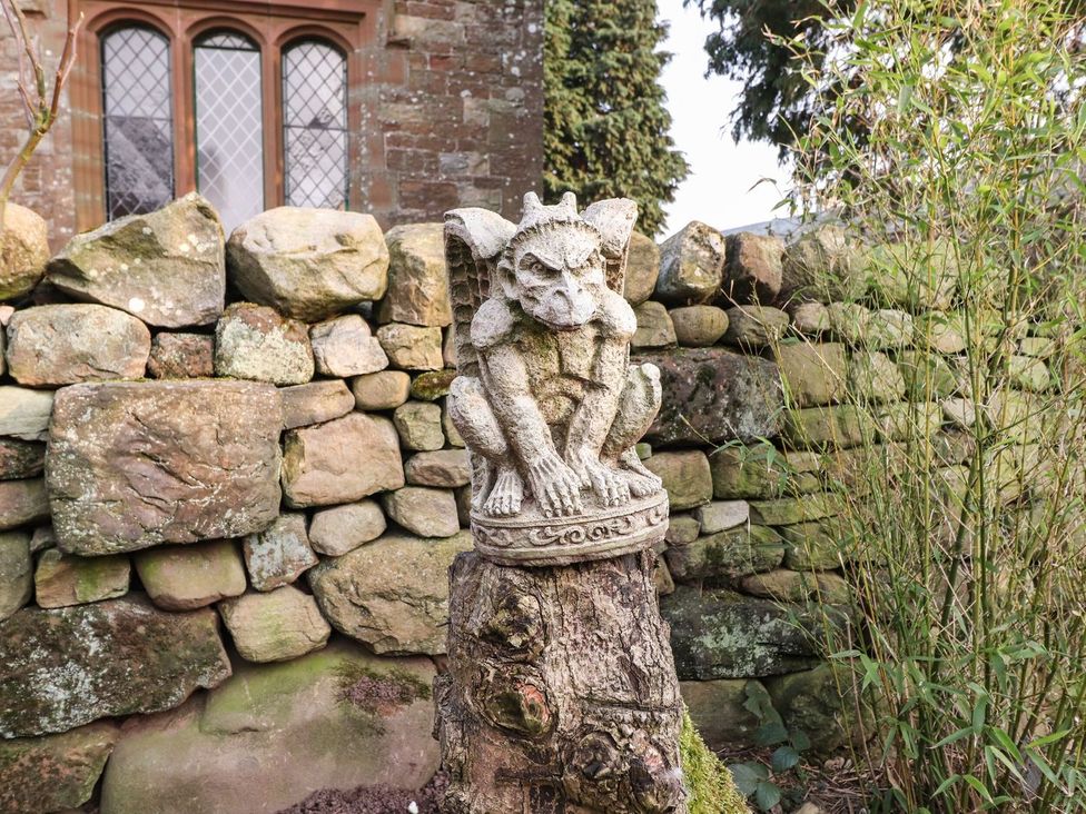 A stone gargoyle statue on a wooden stump near a stone wall at Dunfell Shepherd's Hut in Appleby-In-Westmorland