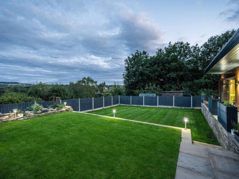 A garden with grass, fence, trees, and lights at The Luxury Shed in Huddersfield