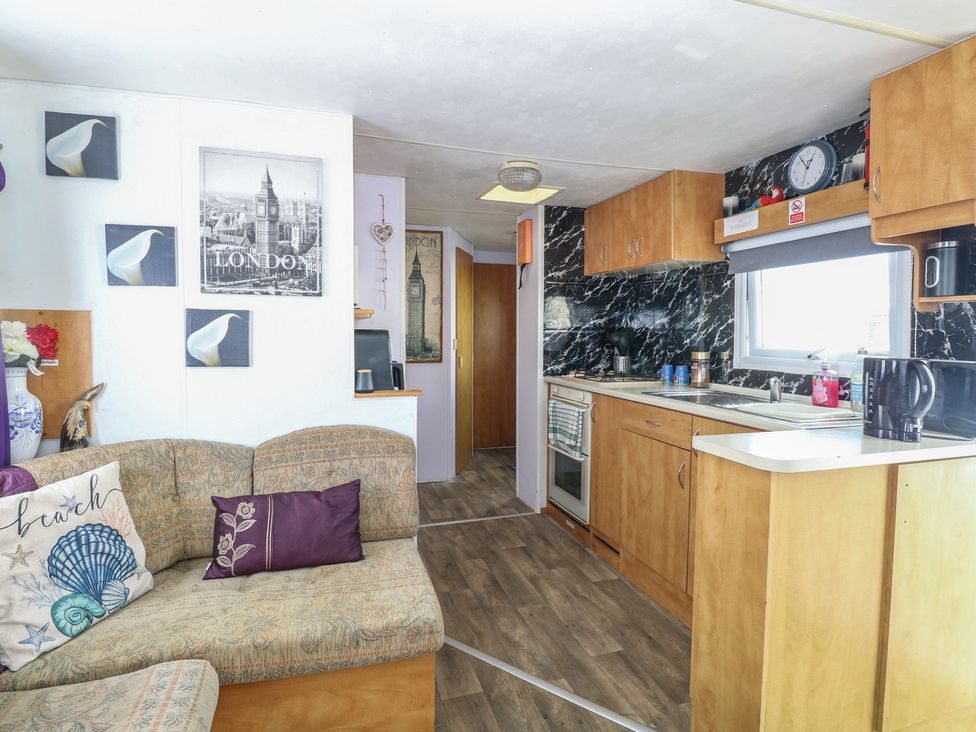 A living room with a sofa and kitchen area at Whispering Meadows - 104 Hemsby