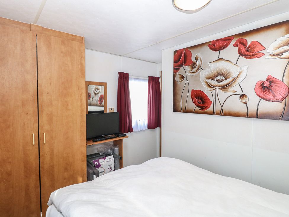 A bedroom with a bed, wardrobe, and television at Whispering Meadows - 104 Hemsby