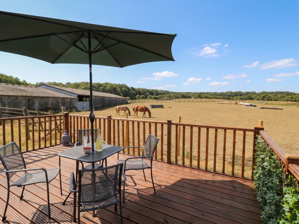 A deck with a table and chairs overlooking horses at Cabin In The Woods in Silverstone