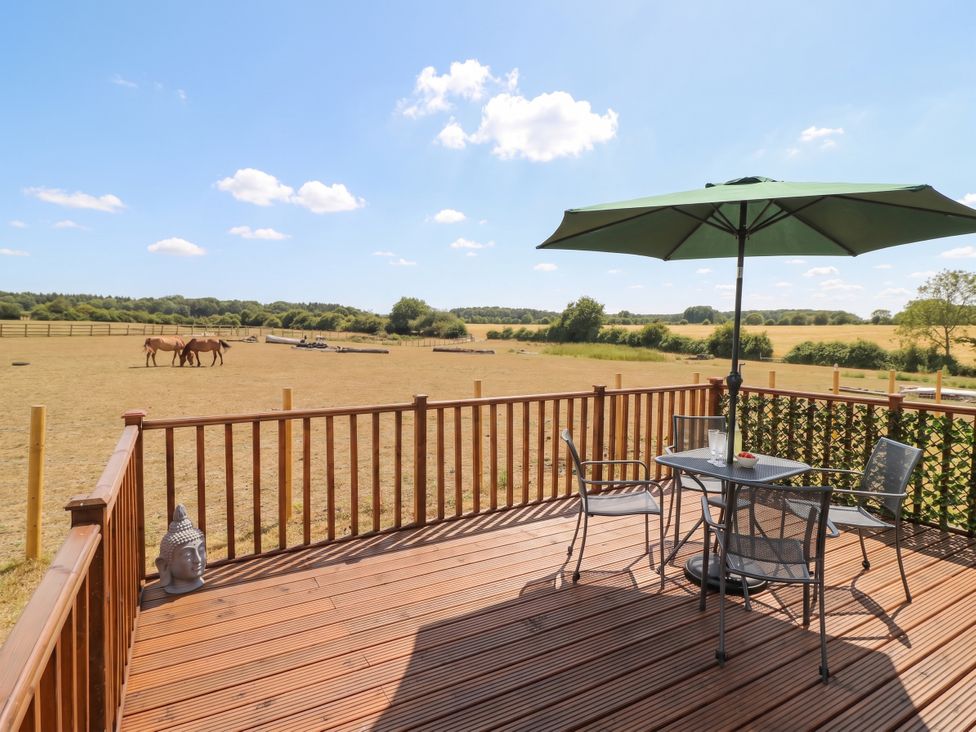 An outdoor area with a deck, table, and horses at Cabin In The Woods Silverstone