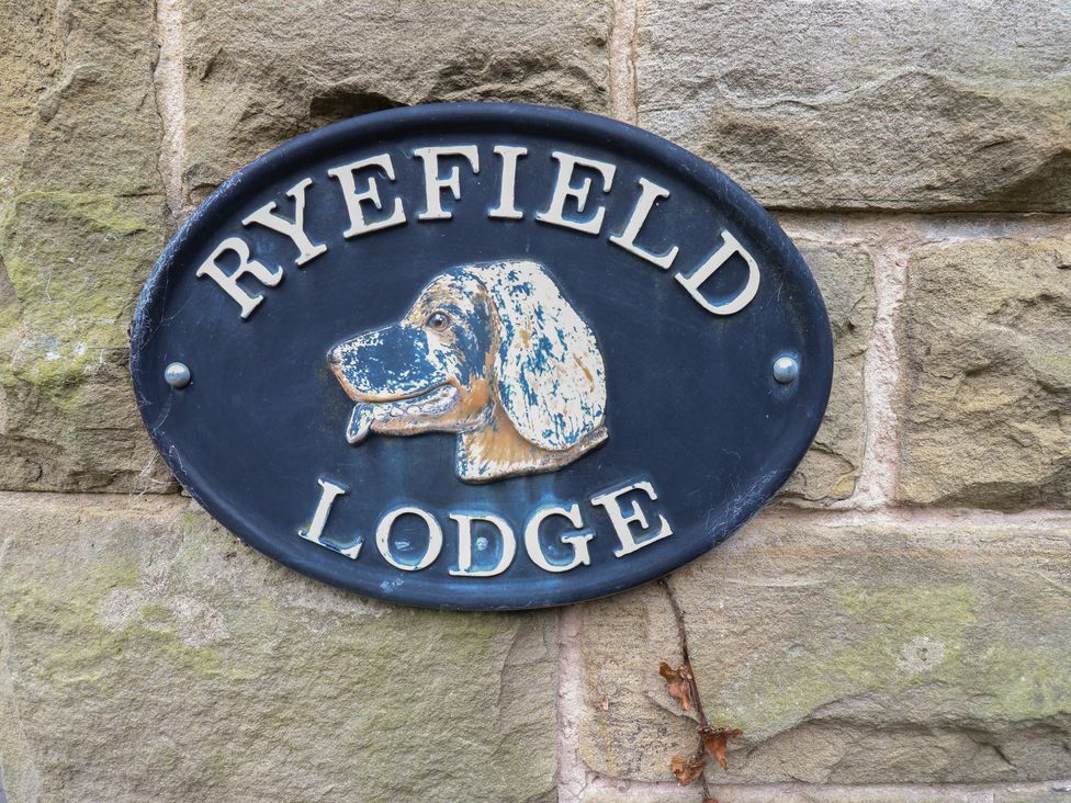 A sign with a dog illustration and the text Ryefield Lodge on a stone wall