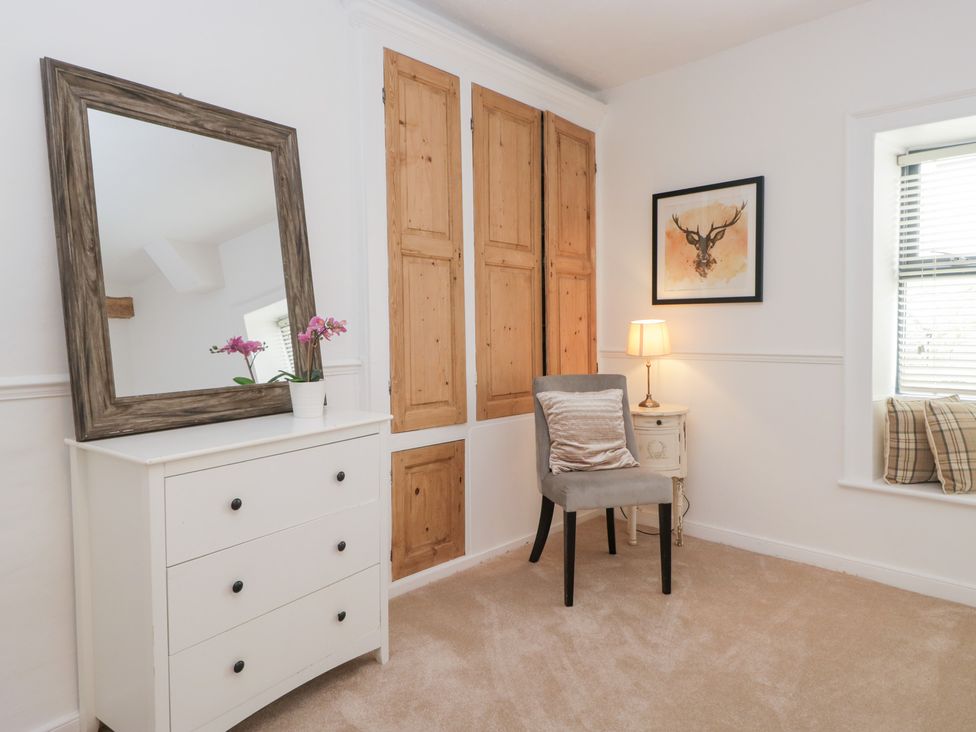 A bedroom featuring a mirror, chest of drawers, chair, and framed artwork at No.2 The Flags, Grange-over-Sands