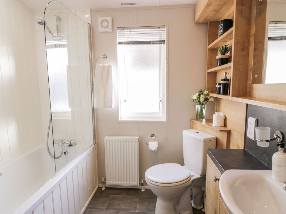A bathroom with a bathtub, toilet, sink, and shelves at Serenity Lodge Wemyss Bay
