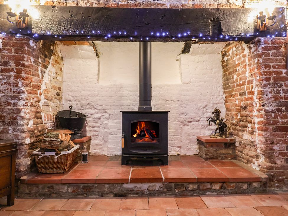 A living room with a wood stove and firewood at Driftway Cottage in Diss