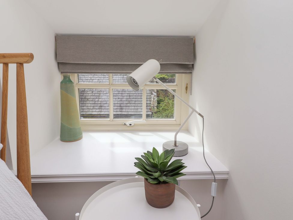 A bedside table with a lamp and plant near a window at Snowdrop Cottage near Warkworth