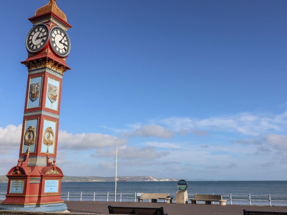 A clock tower by the ocean with benches along the pathway at Flat 7 Weymouth