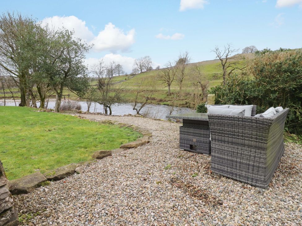 A garden with a river, grass, and outdoor seating at Kirk Yett in Skipton