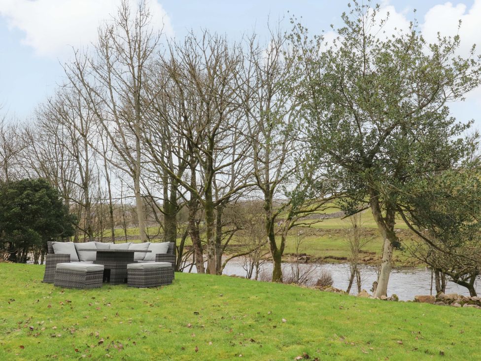 A garden with a sofa and cushions near a river at Kirk Yett in Skipton