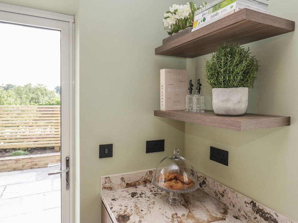 A kitchen corner with a shelf and cookies under a glass dome at Low House Cottage Ayside near Newby Bridge