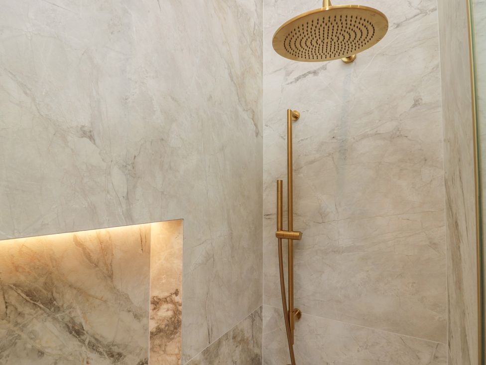 A shower with a rainfall shower head and marble wall panels at Low House Cottage Ayside near Newby Bridge