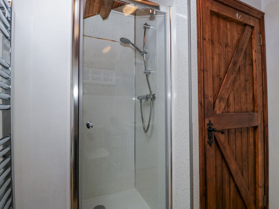 A shower with glass enclosure and wooden door at The Wren's Nest in Ross-on-Wye