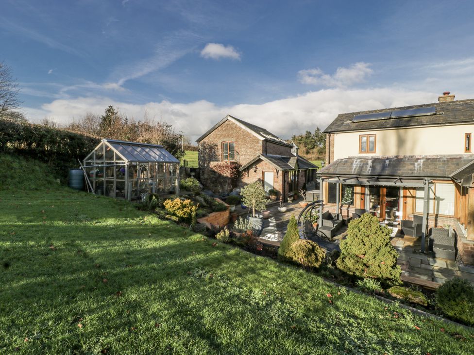 A garden with a greenhouse and seating area at The Wren's Nest in Ross-on-Wye