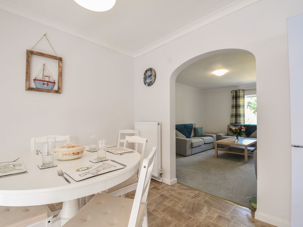 A dining room with a table and chairs leading to a living room at Jazmine in Dacre