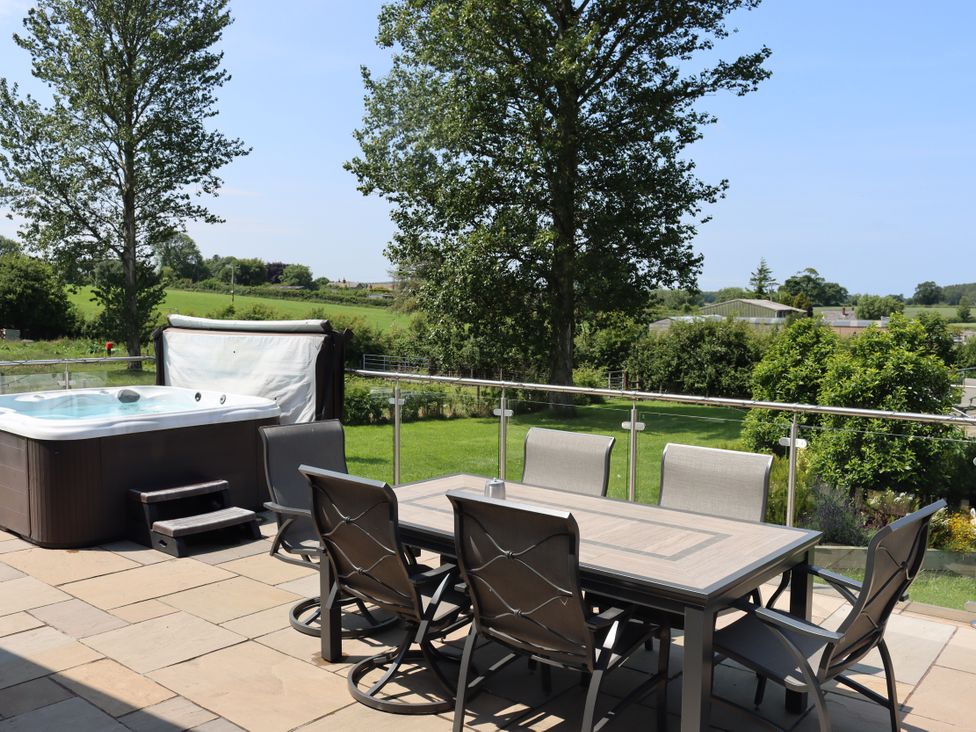 An outdoor area with a hot tub and dining table at Holly Lodge in Lloc near Caerwys