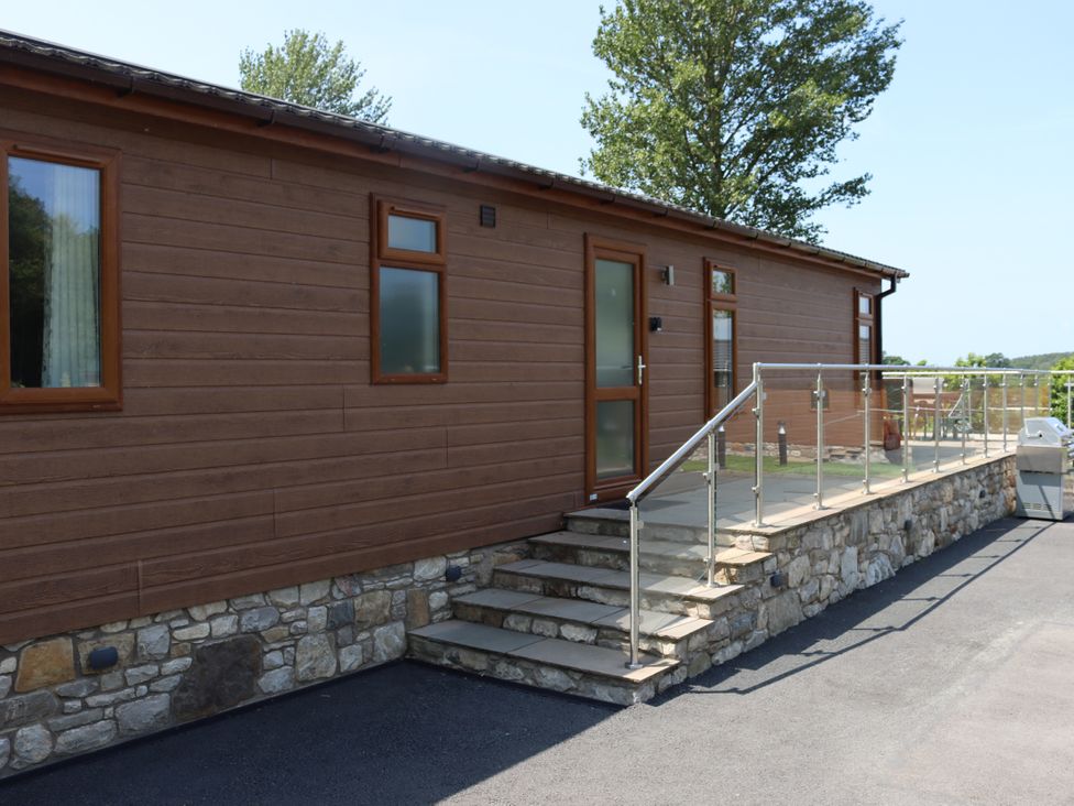 An outdoor view of a wooden lodge with steps and railing at Holly Lodge Lloc near Caerwys