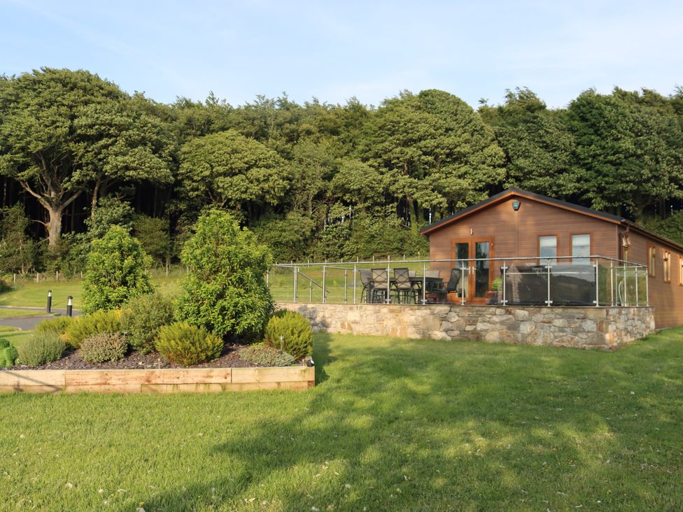 A cabin with a deck and seating area in a garden at Holly Lodge in Lloc near Caerwys