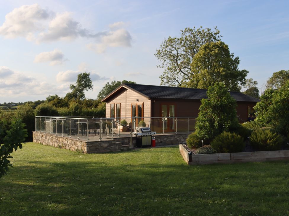 A lodge with a deck and grill in a garden at Pine Lodge near Caerwys