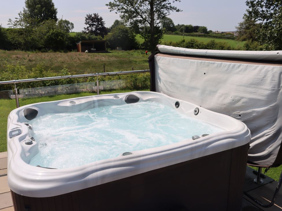 A hot tub on a deck with grass and trees in the background at Pine Lodge in Lloc near Caerwys