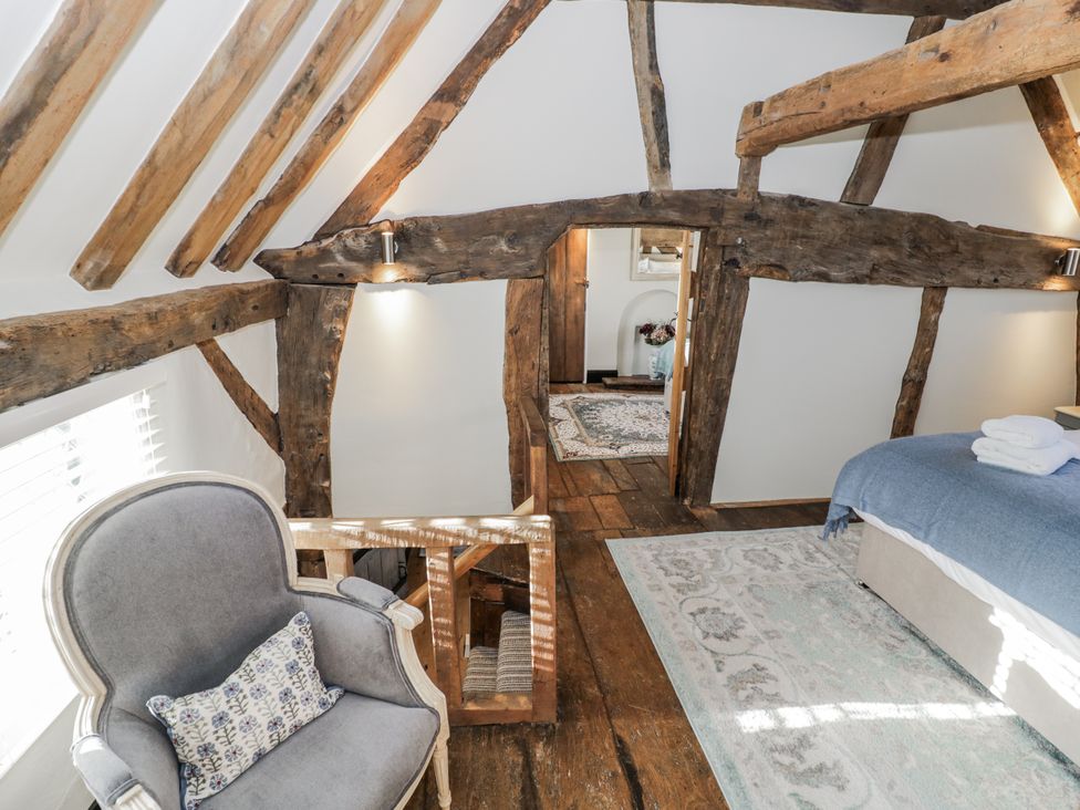 A bedroom with wooden beams and an armchair at Weston Cottage Stratford-upon-Avon