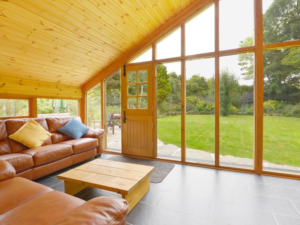 A conservatory with a sofa and wooden table at The Cider Barn at Home Farm Down Thomas near Wembury