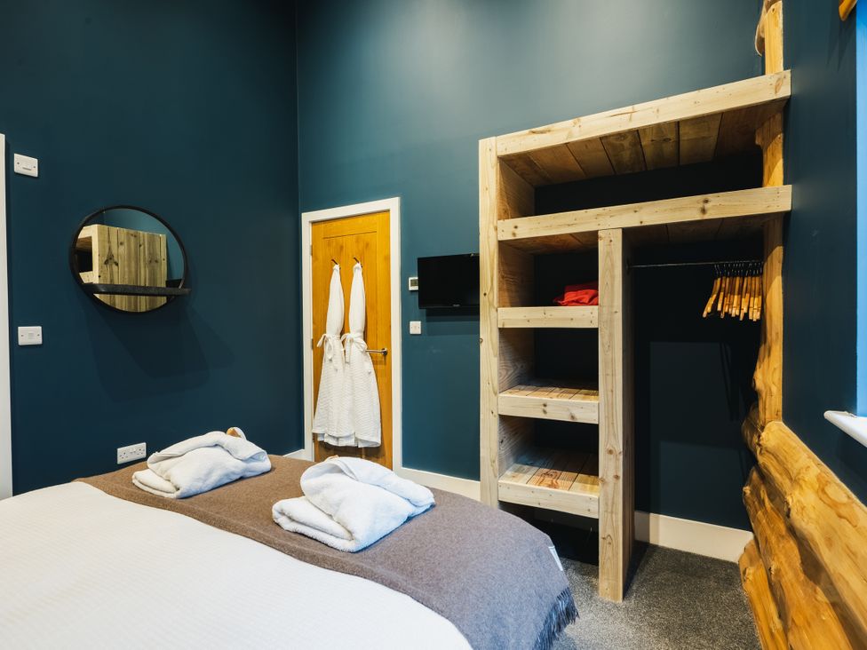 A bedroom with a bed, wooden shelf, mirror, and hangers at The Farmhouse in Addingham